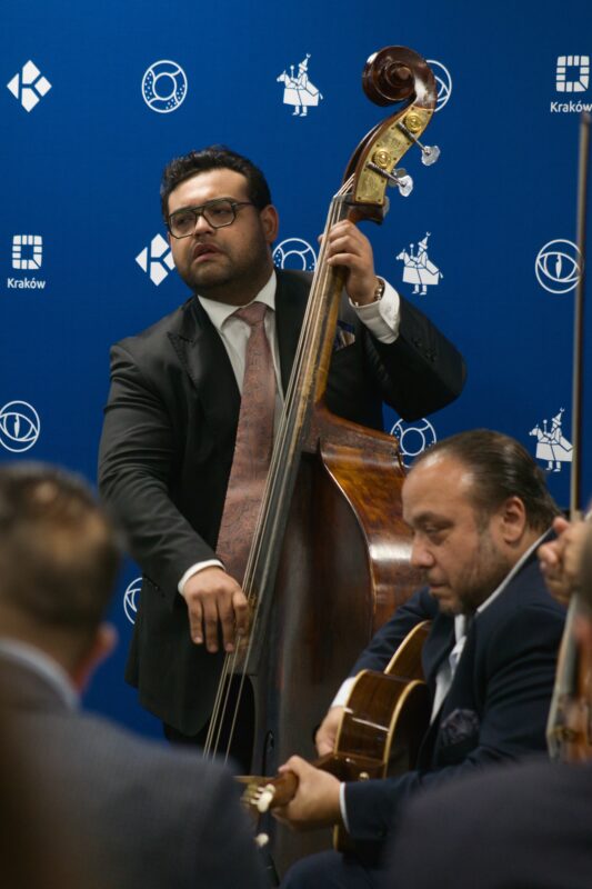 muzycy grający na kontrabasie i gitarze, tło niebieskie z logotypami Krakowa