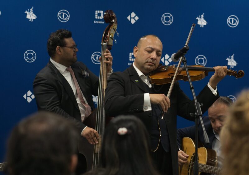 muzycy grający na kontrabasie i skrzypcach i gitarze, tło niebieskie z logotypami Krakowa